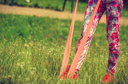 Young woman exercises outdoor in park, using gym accessory, resistance band. Staying fit and healthy.の写真素材