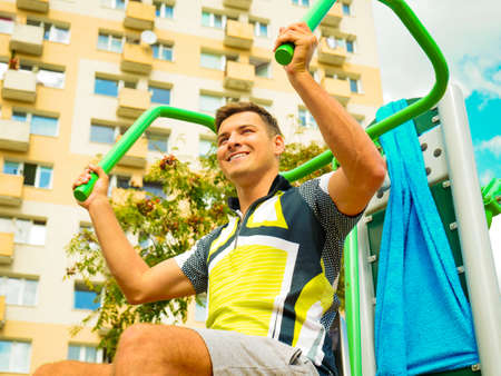 Young handsome man working out in outdoor gym. Sporty guy flexing his muscles on machine. Staying...