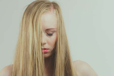 Sad young woman covers her face with long blond hair.の写真素材