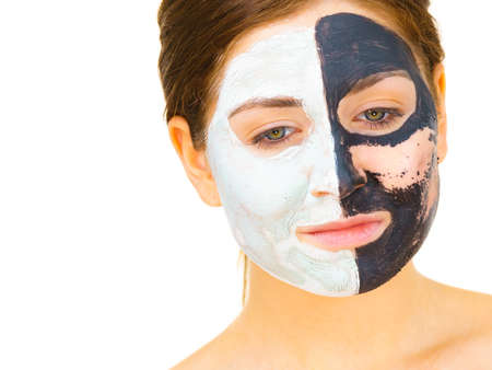 Woman with clay carbo black mask on one half face and white mud on second half. Girl removing cosmetic scrab. Female taking care of oily complexion. Skincare.の写真素材