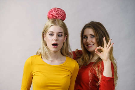 Two young women female student girls thinking about solving problem, holding fake brain. Blonde girl...