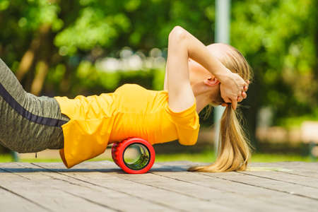 Young woman exercises in park, using gym accessory, foam roller for muscle massage. Staying fit and healthy.の写真素材