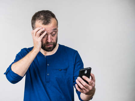 Sad, worried, anxious adult bearded man looking at his smartphone. Guy having problem with technology, being confused after checking social media, front camera.の写真素材