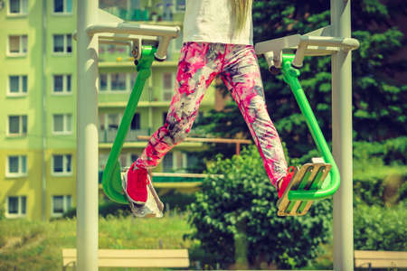 Woman training on sport machine in city park. Female legs exercises on street simulator. Sports equipment in public place.の写真素材