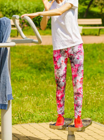Woman training on sport machine in city park. Female legs exercises on street simulator. Sports equipment in public place.の写真素材