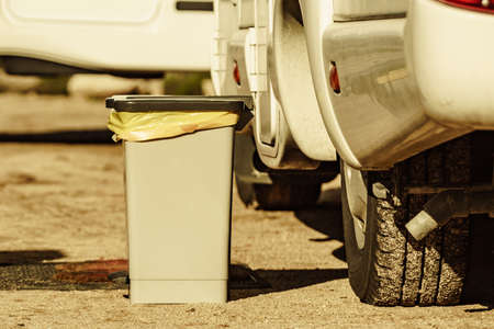 Trash can with plastic bag inside in front of caravan. Holidays and travel in motorhome.