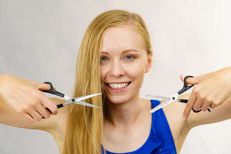 Haircut coiffure haircare concept. Young blonde long hair woman holding scissors showing work tools normal and thinning shears.の写真素材