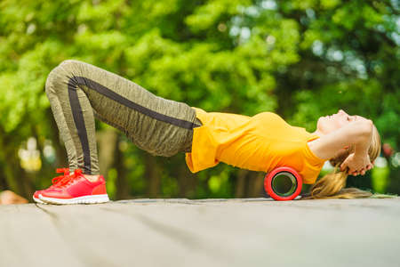 Young woman exercises in park, using gym accessory, foam roller for muscle massage. Staying fit and healthy.の写真素材