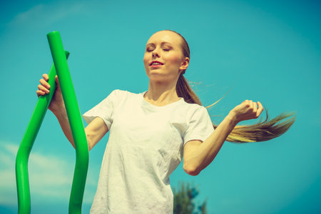 Young woman making exercises on public equipment in city park. Girl working out training in outdoor gym. Healthy lifestyle.の写真素材