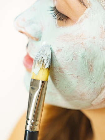 Skin care. Female applying green purifying mud mask, cosmetic healing clay to face, using brush. Beauty and wellness. Spa and acne treatment.の写真素材