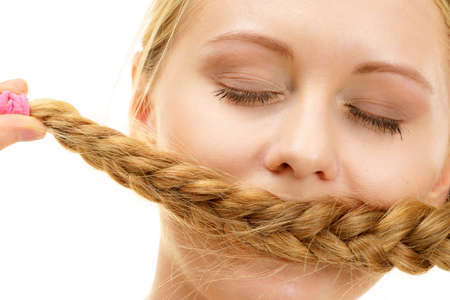 Blonde girl closed eyes covering her mouth with long braid hair. Haircare, hairstyling.