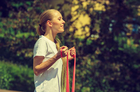 Young woman exercises outdoor in park, using gym accessory, resistance band. Staying fit and...