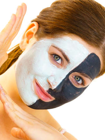 Woman with clay carbo black mask on half face and white mud on second half. Girl taking care of oily...