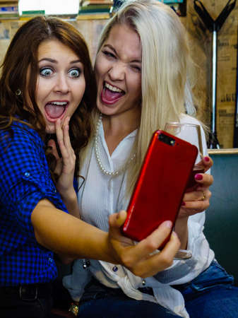 Happy girls best friends drinking alcohol in night club, gossiping, talking and taking self photo...