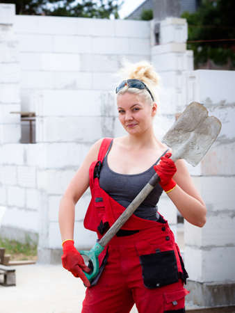 Woman worker using shovel standing on industrial construction site, working hard on house renovation.の写真素材