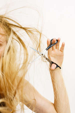 Young woman holding shears tool ready to hair trimming. Blonde female with scissors creating new...