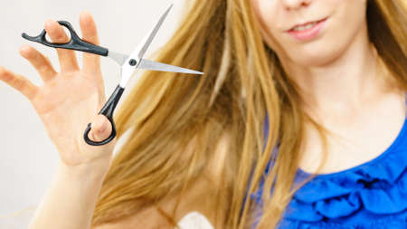 Young woman holding shears tool ready to hair trimming. Blonde female with scissors creating new hairdo coiffure. Hairstyle and haircut.の写真素材