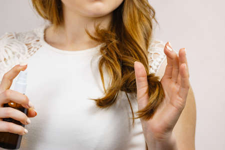 Female model with shiny wavy brown long hair using cosmetic, thermal protect spray. Treatment with oil essence, care and spa procedures. Smooth hairstyle.の写真素材