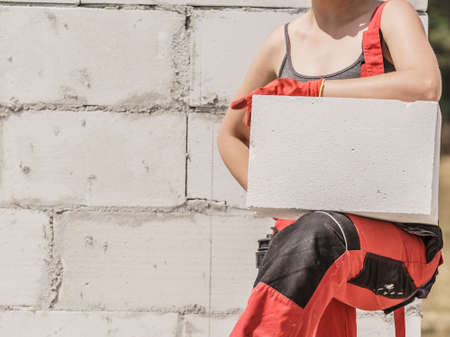 Unrecognizable woman working on construction site, building house, installing white air bricks....