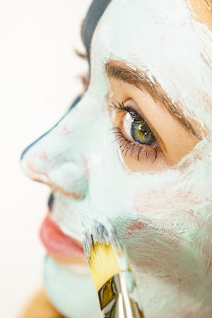 Skin care. Female applying green purifying mud mask, cosmetic healing clay to face, using brush. Beauty and wellness. Spa and acne treatment.の写真素材