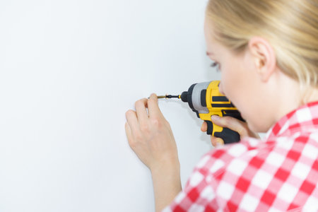 Woman holding yellow driller about to drill something. Hardware construction site objects concept.の写真素材