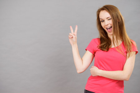 Young happy excited woman winking, doing victory gesture sign. Satisfaction success and celebrating.の写真素材
