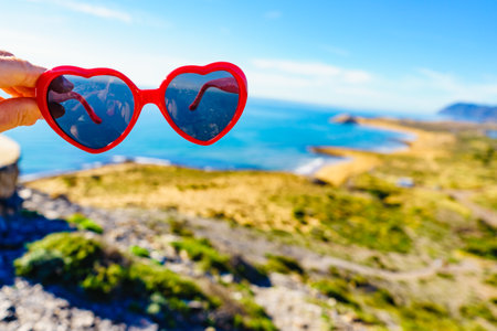 Hand holding sunglasses against spanish sea coast. Travel and holidays.