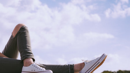 Trendy fashionable unrecognizable woman relaxing outdoor wearing casual footwear white sneakers and hole trousersの写真素材