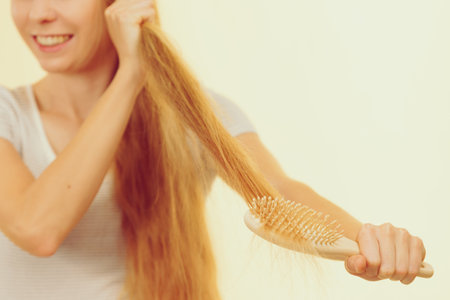 Blonde woman with brush combing her very long messy hair. Teenage girl with bad hair care.の写真素材