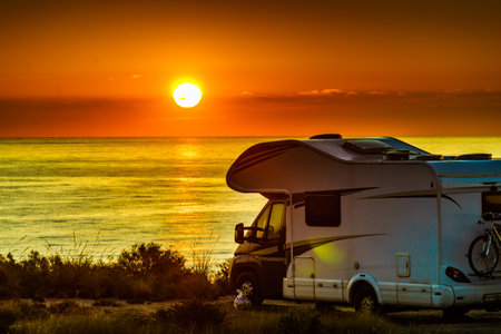 Sun rising over sea horizon, day break and caravan parking on beach sea shore. Travel with mobile homes.の写真素材