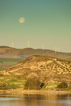 Wind turbines on hills. Full moon on sky at morning. Power generator farm for clean renewable electric energy production near Ardales, province Malaga, Andalusia Spain.の写真素材