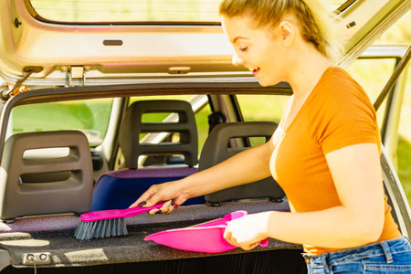 Woman cleaning car interior, using broom and shovel