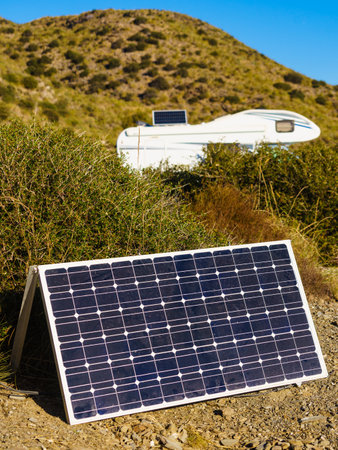 Portable solar photovoltaic panel and camper vehicle in the distance with tilt charging battery on...