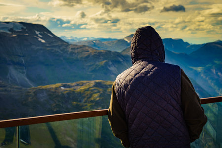 Tourist standing on Dalsnibba viewpoint, Geiranger Skywalk platform, enjoying mountains view,...