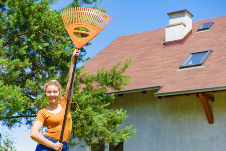 Happy woman working on her backyard, using gardening tools, holds orange rake.の写真素材