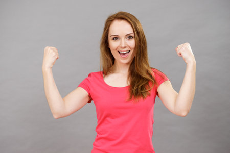 Happy positive woman with arms up clenching fists of joy. Female showing her happiness. Success, achievement, winning concept. Positive emotionsの写真素材