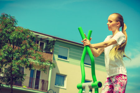 Young woman doing exercises on public equipment in city park. Girl working out training in outdoor gym. Healthy lifestyle.の写真素材