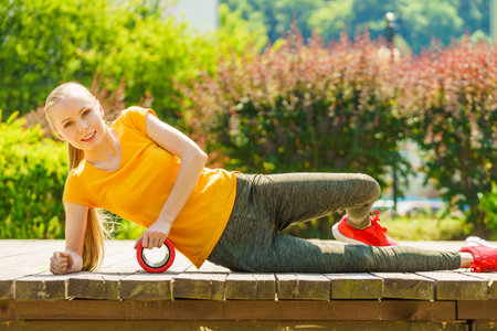 Young woman exercises in park, using gym accessory, foam roller for muscle massage. Staying fit and healthy.の写真素材
