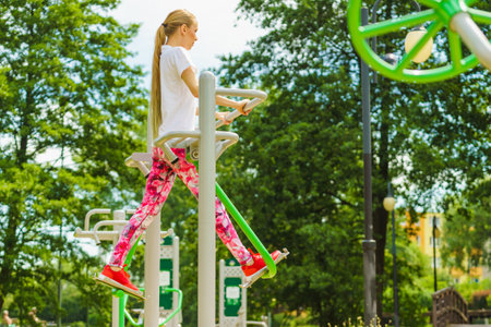 Full body of woman working out in outdoor gym. Girl doing legs exercises on street public equipment on sunny dayの写真素材