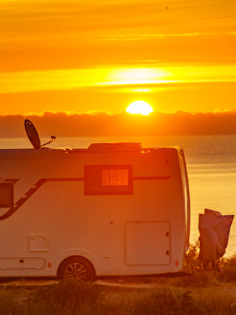 Sun rising over sea horizon and camper rv camping on beach seashore. Holidays in Spain, travel with...