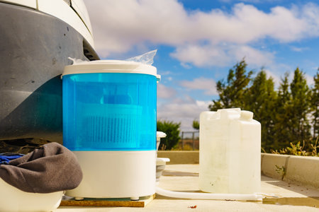Doing laundry on vacation trip. Bowls with clothes and washing machine working. Caravan vehicle in the background. Camping on campsite.の写真素材
