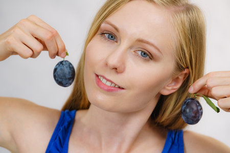 Girl holding blue plum to her ear. Healthy seasonal fruits. Raw food diet. Making jewelry from fruit.の写真素材