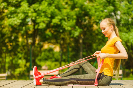 Young woman exercises outdoor in park, using gym accessory, resistance band, strap elastic. Staying fit and healthy.の写真素材