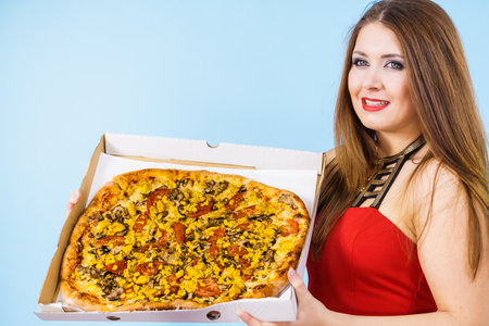 People, italian cuisine concept. Young woman holding hot fresh big pizza in box, on blue. Delicious fast food meal. Delivery service.の写真素材
