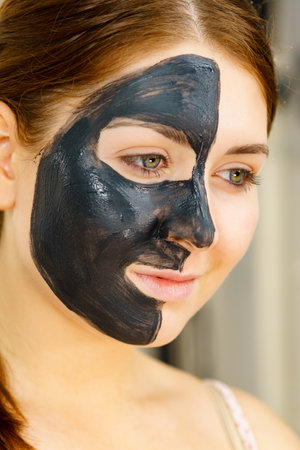 skincare. Woman with charcoal facial mask, deep cleanser on half face. Beauty, spa and acne treatment.の写真素材