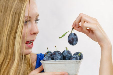 Girl holding blue plum fruits in a paper box. Healthy seasonal fruit, organic nutrition, fresh eating.の写真素材