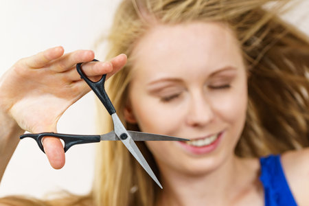 Young woman holding shears tool ready to hair trimming. Blonde female with scissors creating new hairdo coiffure. Hairstyle and haircut.の写真素材