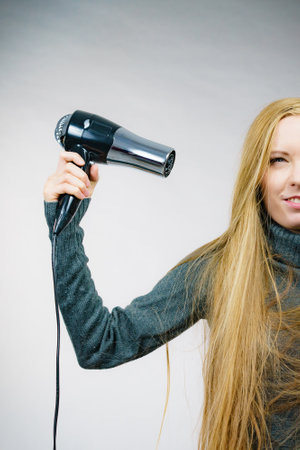 Blonde woman styling her very long hair. Female holding hairdryer. Hair accessories.の写真素材