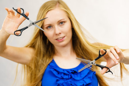 Haircut coiffure haircare concept. Young blonde long hair woman holding scissors showing work tools normal and thinning shears.の写真素材