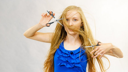 Haircut coiffure haircare concept. Girl with blowing long blond hair holding scissors, showing work tools, normal and thinning shears.の写真素材